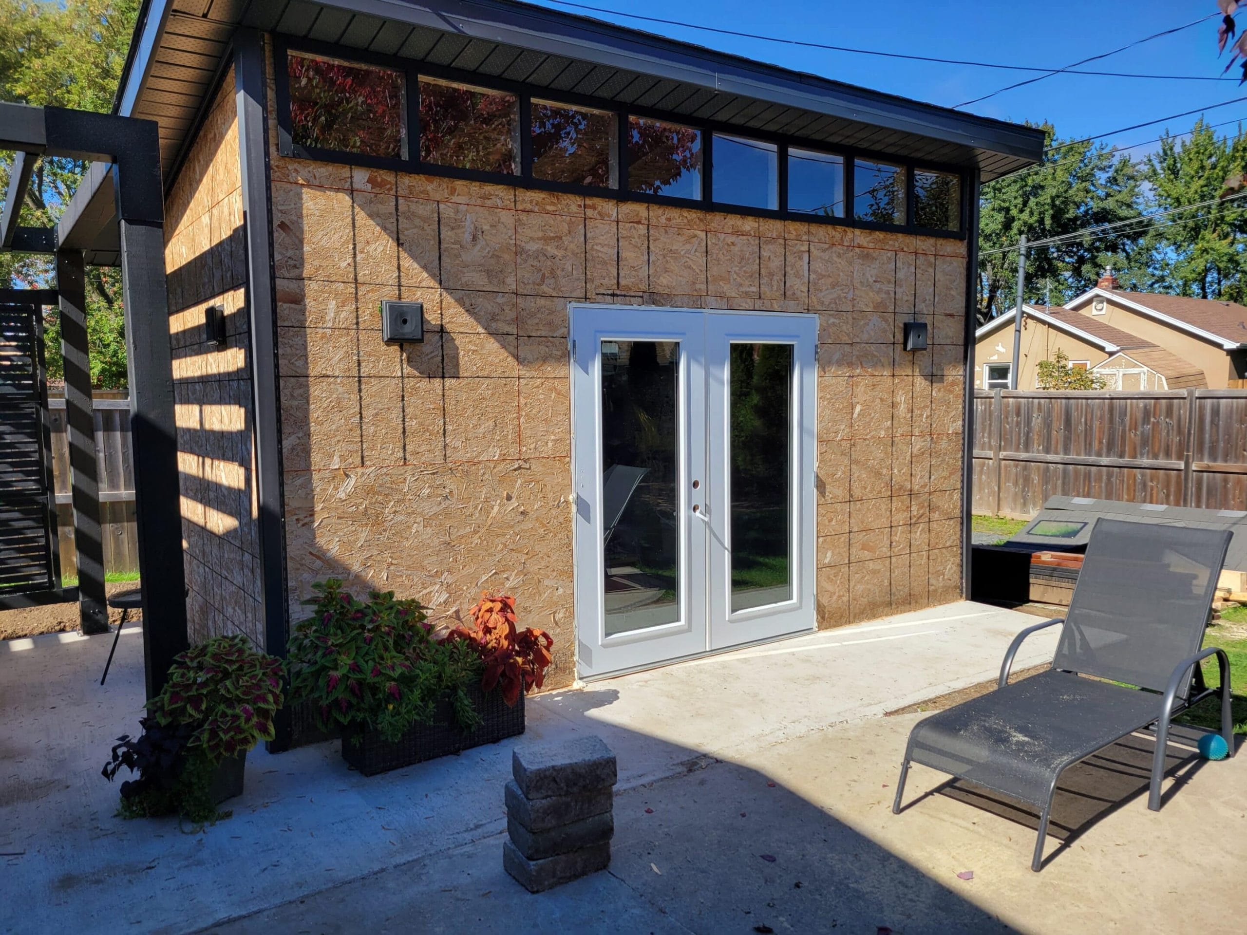 Small backyard shed with patio and lounge chair.